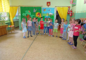 Dzieci w kolorowych ubrankach stoją ustawione w półkolu.